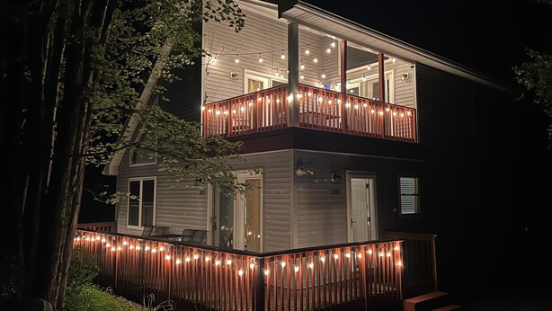 Uma casa de dois andares com varanda, luzes de festa e o número 337 na porta.