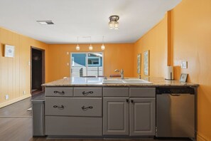A kitchen with a granite countertop, a sink, and a dishwasher. There are three pendant lights above the sink. - SoCo 4BR | 1 Block to South Congress Ave (Austin)