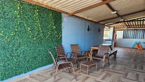 Un espace extérieur aménagé avec des chaises en osier et une table en bois, un mur végétal et un toit en métal ondulé.