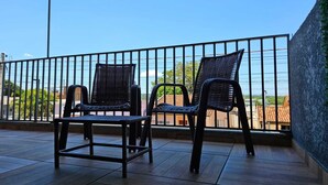 Deux fauteuils en osier sur un balcon, avec vue sur des immeubles et de la verdure.