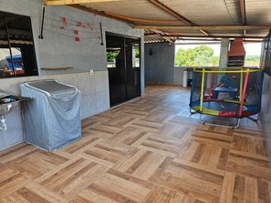 Un espace intérieur spacieux doté d’un parquet en bois disposé en point de Hongrie, un espace extérieur couvert avec des sièges et une cheminée visible.