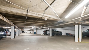 Eine mehrstöckige Parkgarage mit Betonpfeilern, Deckenbeleuchtung und mehreren parkenden Fahrzeugen.