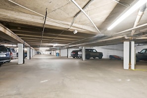 Eine mehrstöckige Parkgarage mit Betonpfeilern, Deckenbeleuchtung und mehreren parkenden Fahrzeugen.