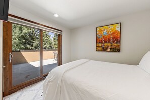 A bedroom with a bed, a painting, and a sliding glass door leading to an outdoor area. - Spacious Vail Golf & Ski Condo, Pool, Hot Tub (Vail)