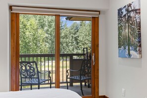 A room with a bed, a sliding glass door leading to an outdoor area with chairs and a view of trees. - Spacious Vail Golf & Ski Condo, Pool, Hot Tub (Vail)