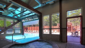 Ein Wellnessbereich mit Whirlpool, einer Glastür und Blick auf Pool und Sitzgelegenheiten im Freien.