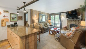 Ein Wohnzimmer mit Kamin aus Stein, Fernseher, einer Couch und einer Küchenzeile mit einer Granitarbeitsplatte.