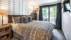 Ein Schlafzimmer mit Bett, Nachttisch, Lampe und Blick ins Freie.