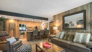 Ein modernes Wohnzimmer mit einer Couch, einem Couchtisch und einem Essbereich mit Stühlen, im Hintergrund eine Küche.
