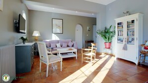 Ein Wohnzimmer mit Sofa, Sesseln, einem Couchtisch, einer Heizung, einem Bücherregal und einem Blumentopf.