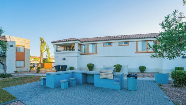 Una casa moderna con un patio que cuenta con una parrilla, asientos y macetas.