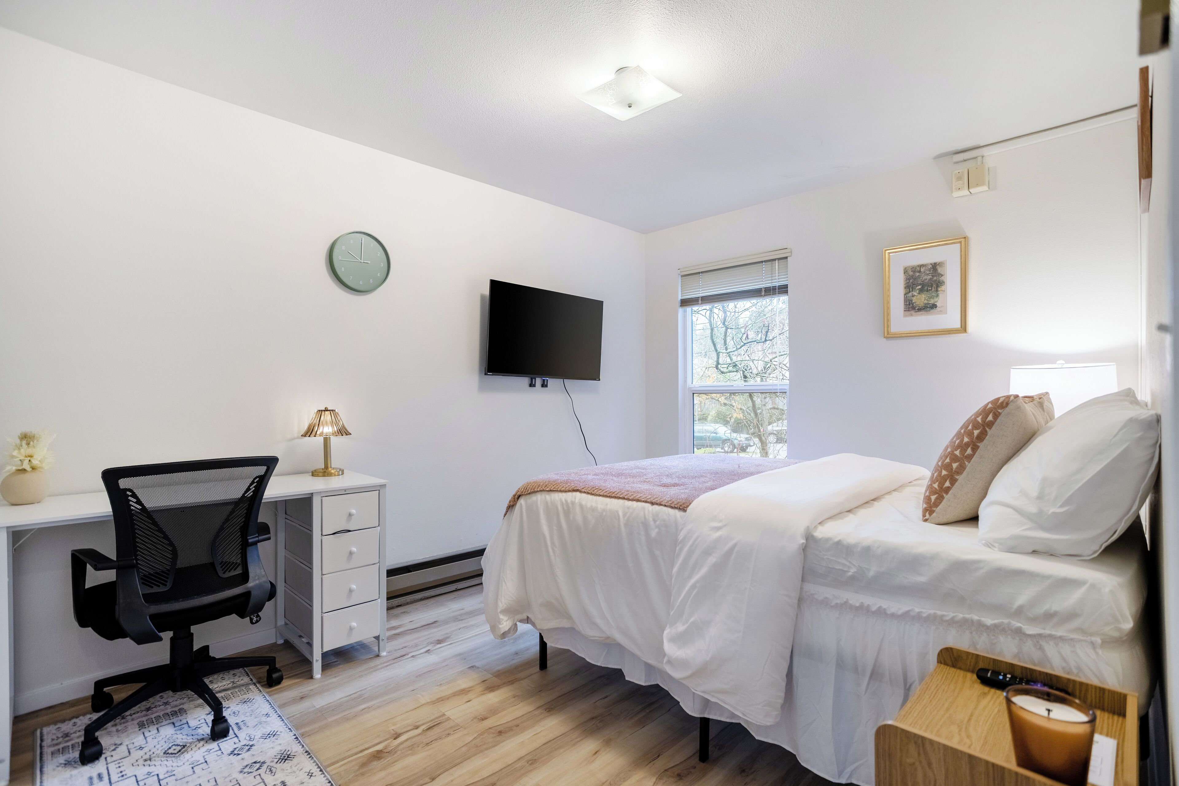 Een slaapkamer met een bed, bureau, stoel, televisie, klok en raam.
