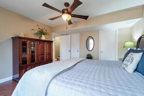 A bedroom with a large bed, a ceiling fan, a dresser, a mirror, and a door leading to another room. - Treehouse Vibes near Lake Coronado (Hot Springs)
