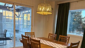 Comedor con mesa y sillas de madera, lámpara colgante y vista a través de puertas de vidrio grandes.