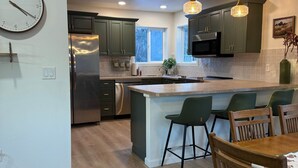 Una cocina moderna con una isla central, gabinetes verdes, electrodomésticos de acero inoxidable e iluminación colgante.