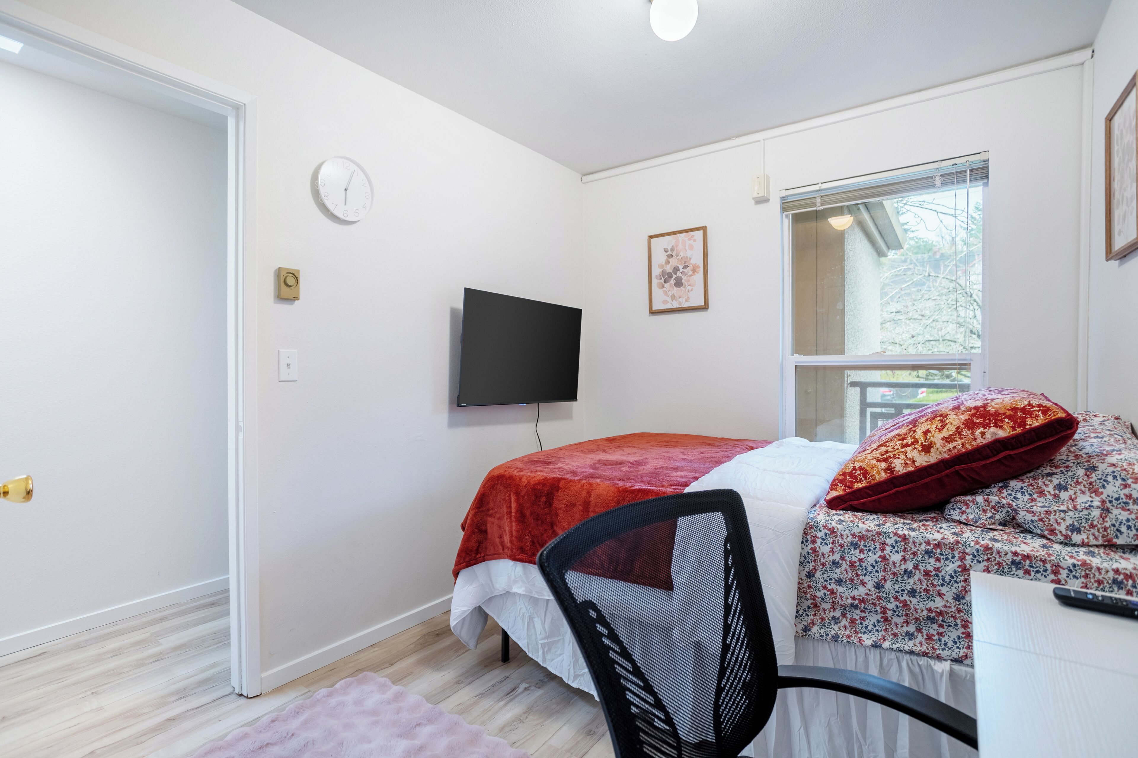 A bedroom with a bed, a chair, a TV, a window, and a door.