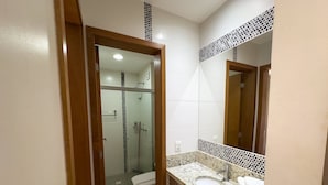 Une salle de bain avec une douche à parois de verre, des toilettes, un lavabo avec un miroir et un mur recouvert de carreaux.