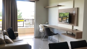 Une chambre d’hôtel moderne équipée d’un canapé, d’une table à manger, de chaises, d’un téléviseur fixé sur une étagère en bois et d’un balcon avec vue.