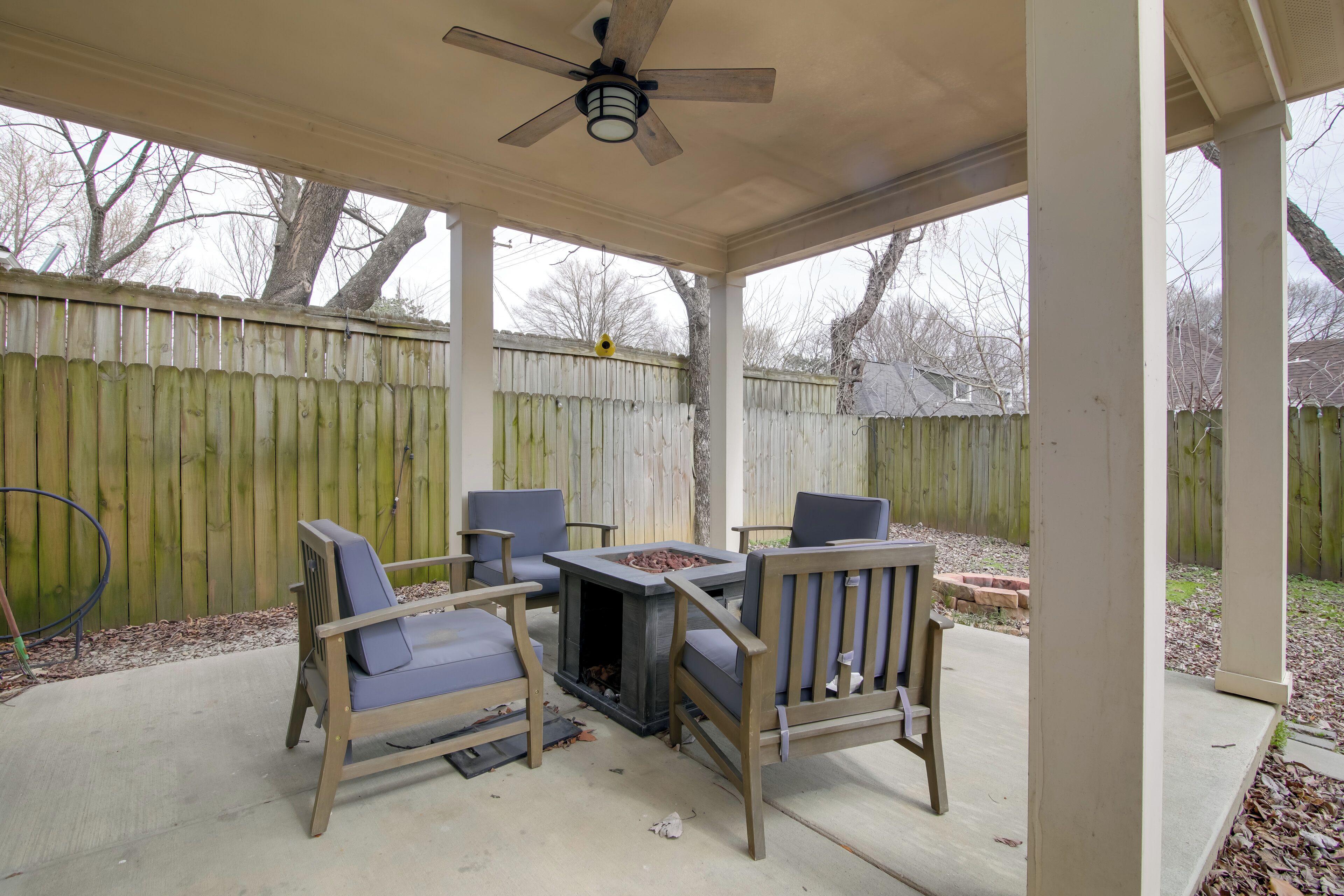 A covered patio with a table and chairs, a ceiling fan, and a wooden fence in the background.