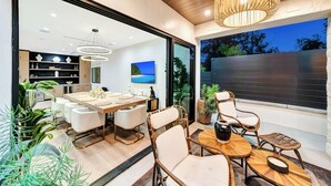 A modern dining area with a wooden table and white chairs, a wicker seating area, and a large window with a view of the outdoors. - private resort excusive villa Tarzana south 6500sq with adu pool spa (Los Angeles)