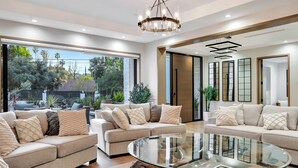 A modern living room with two sofas, a glass coffee table, and large windows offering a view of greenery outside. - private resort excusive villa Tarzana south 6500sq with adu pool spa (Los Angeles)