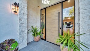 A modern entrance with a stone wall, a wooden door, and potted plants. - private resort excusive villa Tarzana south 6500sq with adu pool spa (Los Angeles)