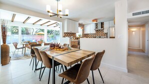 Un comedor amplio con una mesa de madera y sillas marrones, una cocina con armarios blancos y un ventanal que proporciona luz natural.