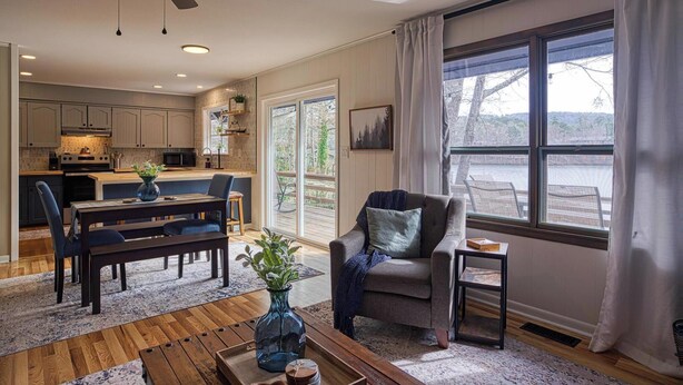 A modern kitchen with wooden cabinets, a dining area with a bench, and a large window with curtains. - 05202 - 3 Guadalajara Lane (Hot Springs Village)