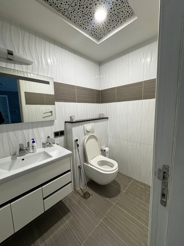 Un baño moderno con lavamanos, espejo y retrete blancos.