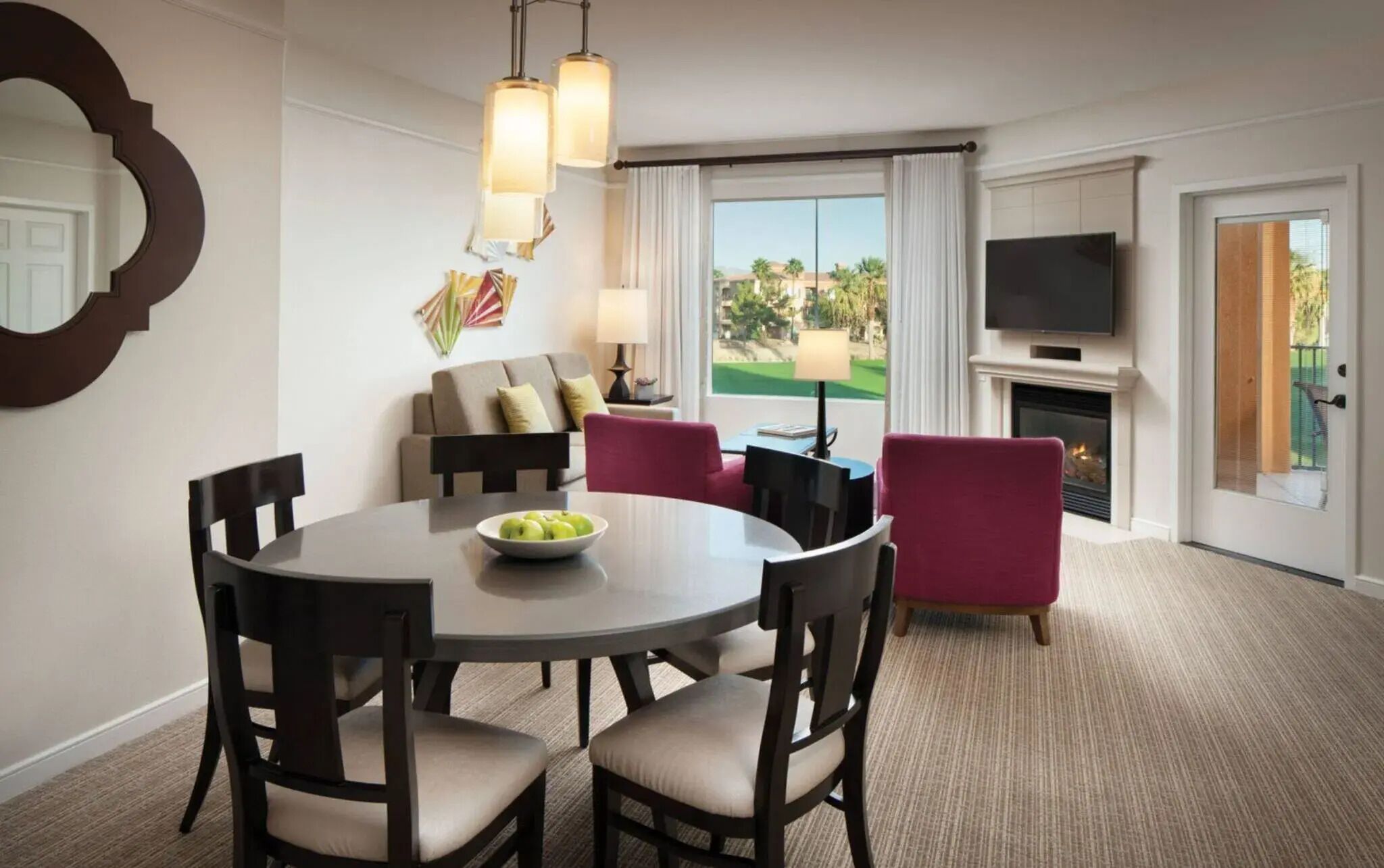 Habitación de hotel con comedor, sofá, televisor y chimenea.