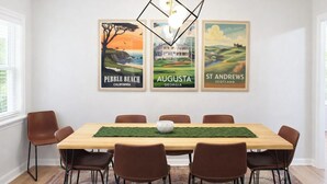 Ein Esszimmer mit einem Holztisch, sechs braunen Stühlen und drei gerahmten Reiseplakaten an der Wand.