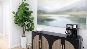 Ein modernes Wohnzimmer mit einem großen Landschaftsbild, einer Kaffeemaschine und einem Topfpflanzen.