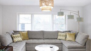 Ein Wohnzimmer mit einer grauen Eckcouch, einem runden Couchtisch und einem großen Fenster mit Jalousien.