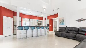 Een moderne woonkamer met een zwarte leren bank, een keuken met rode accenten, en een barruimte met blauwe stoelen.