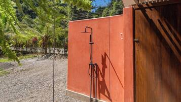 A red structure with a showerhead, a gravel ground, and a wooden door.