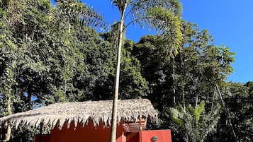 A small red building with a thatched roof, surrounded by dense tropical foliage.