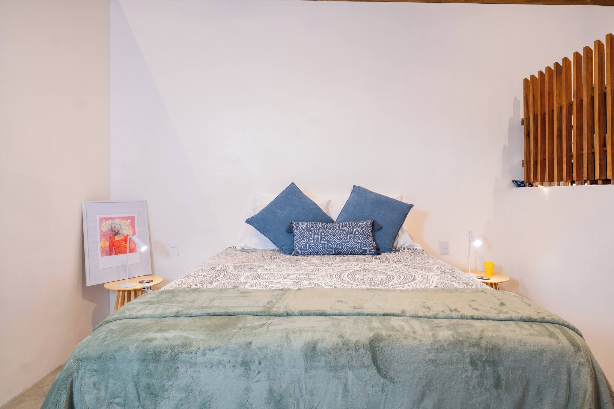 A bedroom with a bed, pillows, a blanket, a bedside table, a lamp, and a wall-mounted light fixture.