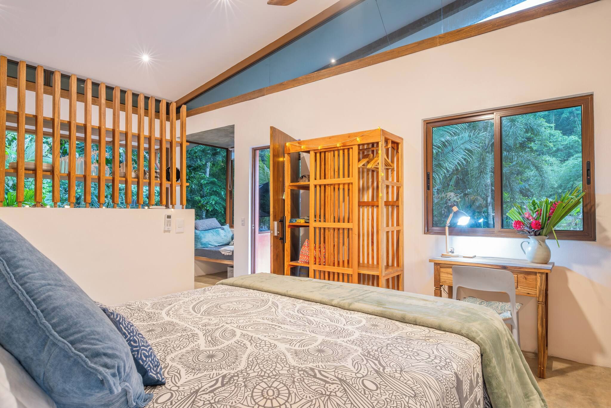 Ein Schlafzimmer mit Bett, Schreibtisch, Bücherregal und einem großen Fenster mit Blick auf Grünflächen.
