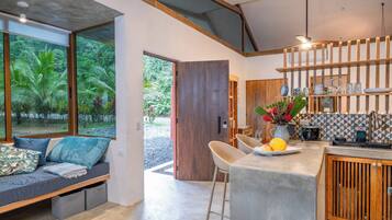 A modern kitchen with a bar area, a seating area with a view of greenery, and a large wooden door.