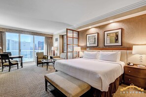 Ein Hotelzimmer mit einem großen Bett, einem Schreibtisch, einem Sessel und Blick auf die Stadt.
