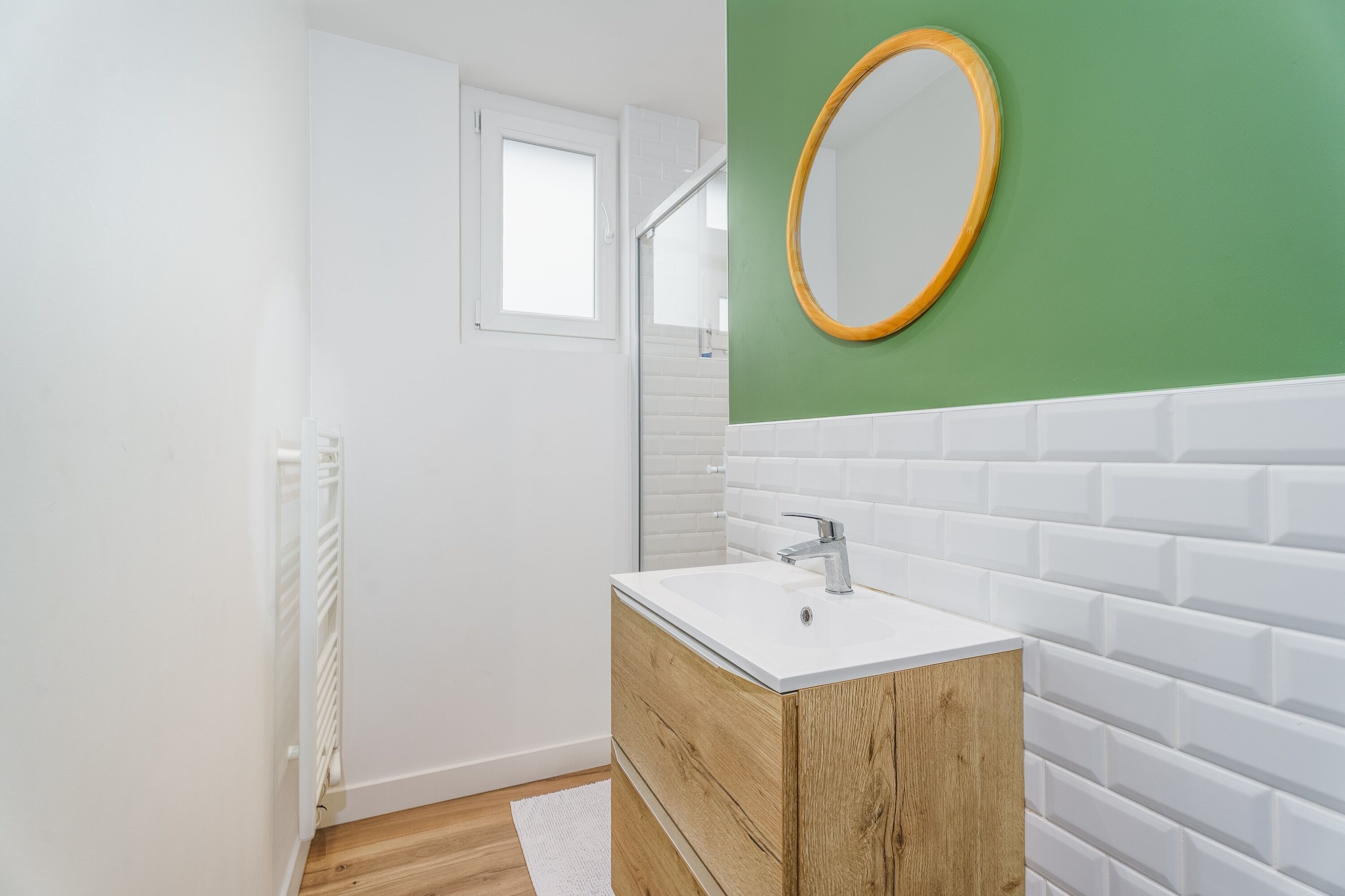 A modern bathroom with a white sink, wooden vanity, and a green accent wall.