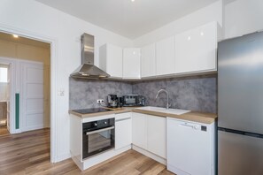 A modern kitchen with white cabinets, a stainless steel range hood, a built-in oven, a dishwasher, and a microwave.