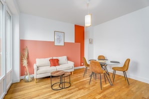 Un salon moderne avec un canapé blanc, une table à manger avec des chaises, un vase contenant des plumes d’herbe des pampas et un tableau encadré accroché au mur.