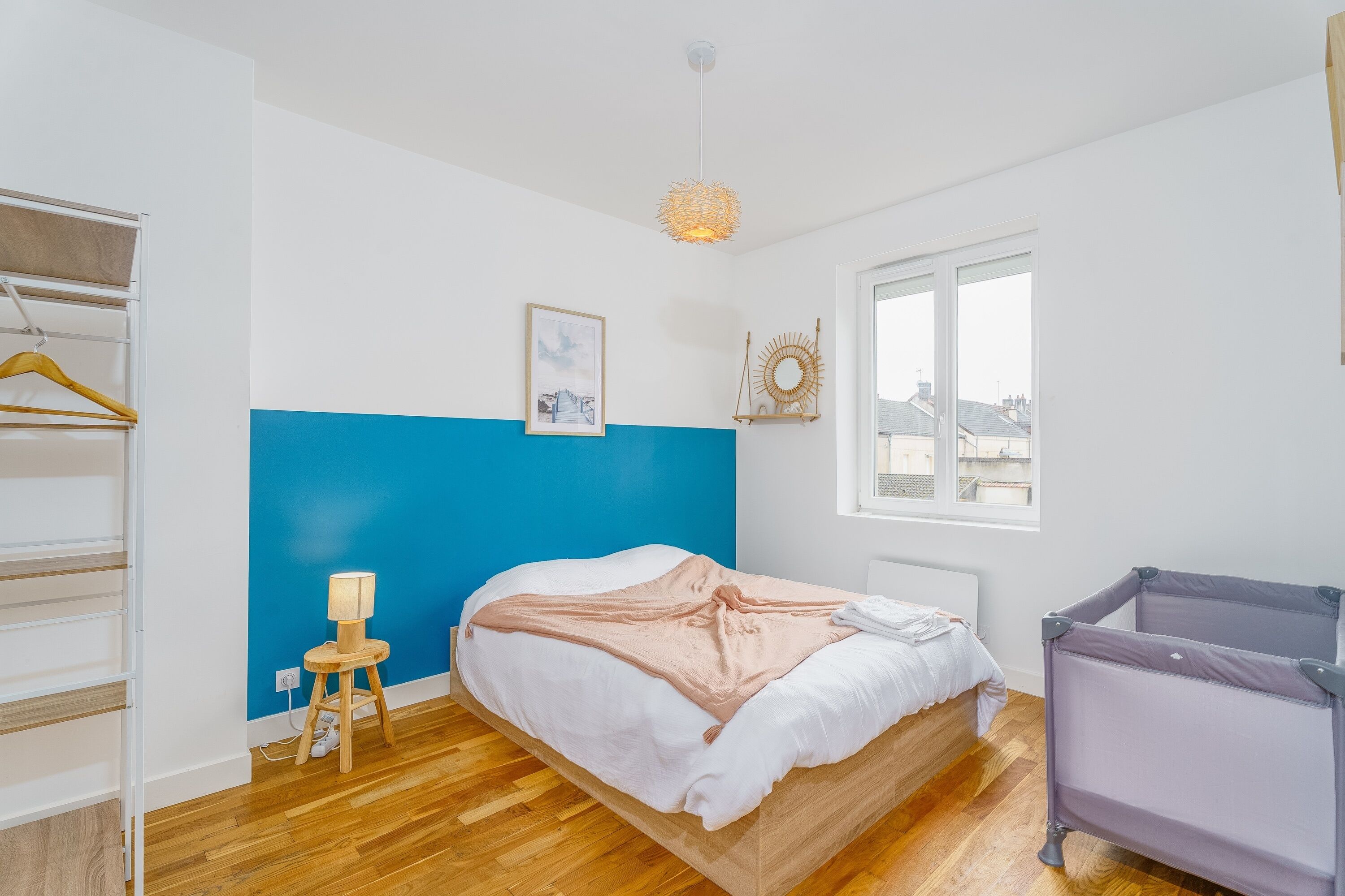 Une chambre à coucher avec un lit, une table de chevet avec une lampe, une fenêtre et un berceau.