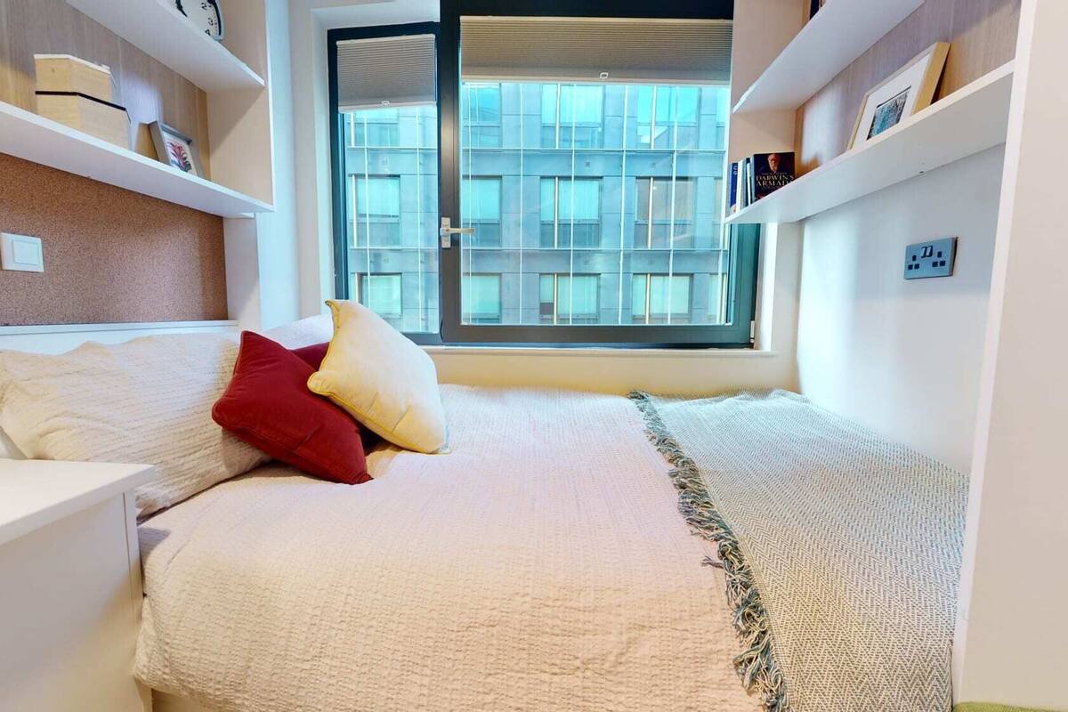 A bedroom with a bed, a window, and a bookshelf.