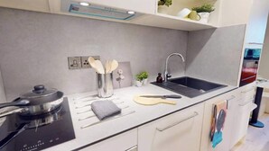 Eine moderne Küche mit integriertem Induktionskochfeld, einem Spülbecken und einer Arbeitsplatte mit Geschirr und einer Gitarre.