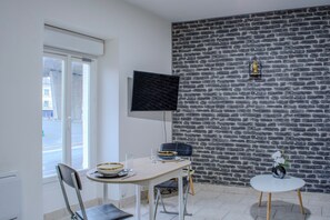 Et moderne spiseområde med en murstensvæg, et fladskærms-tv ophængt over et bord, og et lille rundt bord med en vase.