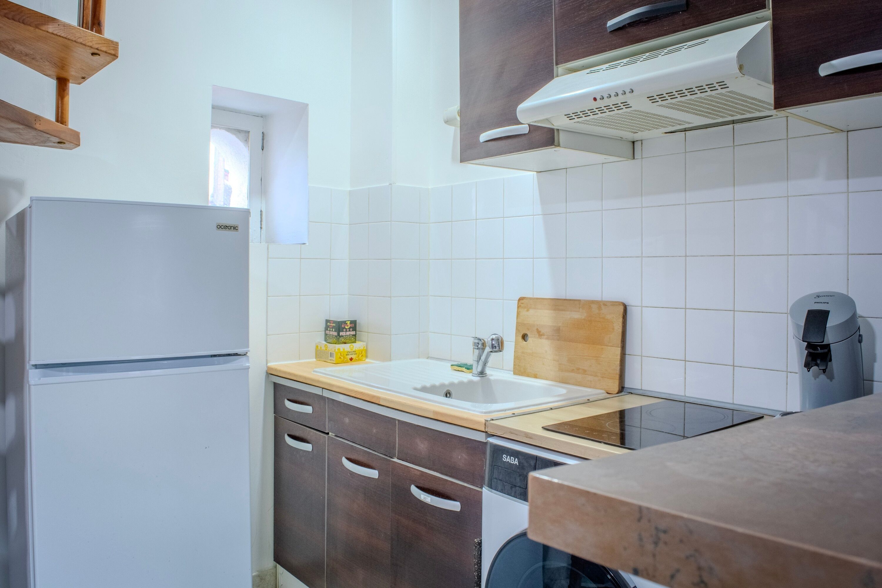 Cocina compacta con refrigerador, lavaplatos, muebles de madera y pileta.