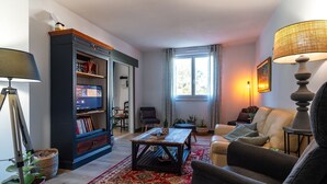 Sala de estar con sofá, sillón, mesa de centro, estantería y televisor.
