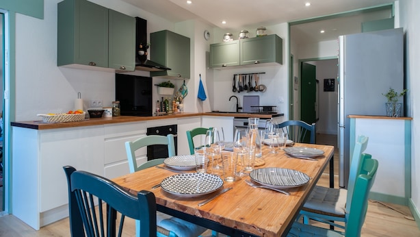 Una cocina moderna con armarios verdes, una mesa de comedor de madera dispuesta para seis comensales y un refrigerador.